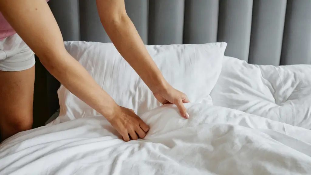 Mulher arrumando e organizando lençóis brancos na cama com cabeceira cinza
