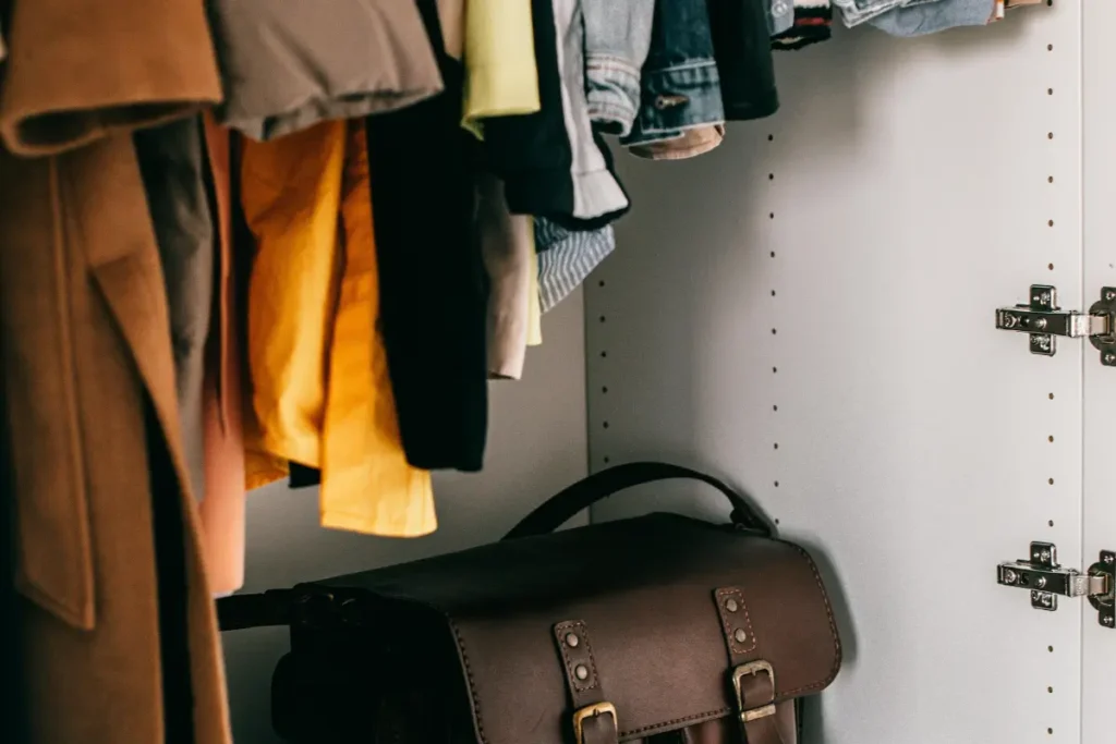 Interior de guarda-roupa com roupas penduradas em cabides e bolsa de couro marrom no chão