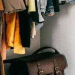 Interior de guarda-roupa com roupas penduradas em cabides e bolsa de couro marrom no chão
