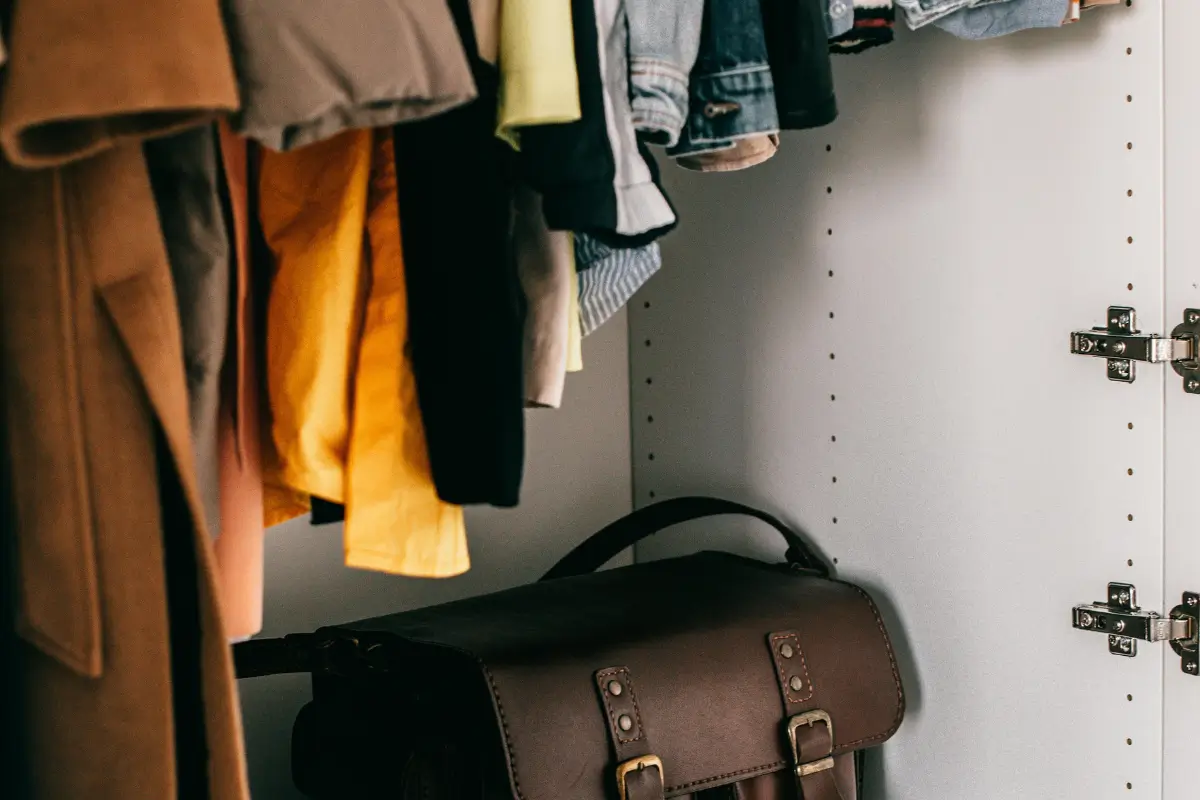 Interior de guarda-roupa com roupas penduradas em cabides e bolsa de couro marrom no chão